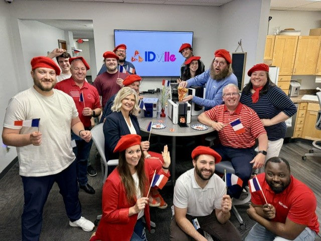 IDVILLE team members wearing red berets and holding French flags during an office celebration.